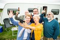 Group of older adults enjoying a day outside a camper, holding drinks and taking a selfie. Smiling and cheerful, they celebrate togetherness and fun. Old friends taking selfie in caravan campsite.