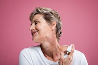 Smiling woman with short hair applying skincare. Mature woman enjoying skincare routine. Happy woman with skincare product against pink background. Anti-aging skincare routine for mature woman.