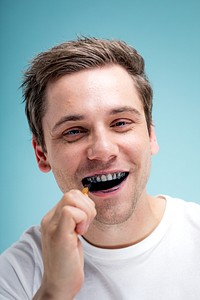 Man brushing teeth with charcoal toothpaste, smiling. Charcoal toothpaste used by man for teeth cleaning. Happy man with charcoal toothpaste on teeth. Man cleaning teeth, dental hygiene.