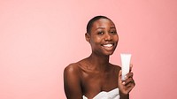 Smiling woman holding skincare product, pink background. Skincare focus with woman displaying product. Happy woman promoting skincare routine. African woman and skincare, holding a beauty cream tube.