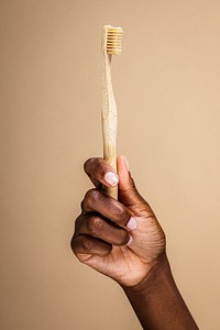 Hand holding a bamboo toothbrush against a beige background. Eco-friendly bamboo toothbrush in a hand. Sustainable bamboo toothbrush for oral care. African woman brushing her teeth, dental hygiene.