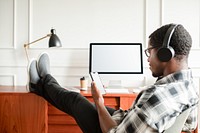 Man relaxing with headphones, using smartphone at desk. Casual work setting with computer. Comfortable, focused, and tech-savvy atmosphere. African American man relaxing, using smartphone by desk.