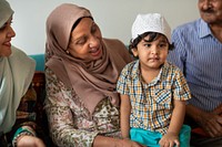 Family gathering. Smiling elderly woman in hijab, young child in plaid shirt and cap. Warm, multicultural family scene, joyful family interaction. Muslim family sitting together on sofa in home.