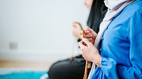 Two muslim women in traditional attire, one in blue, holding prayer beads. Focus on hands and beads, symbolizing prayer and spirituality in a serene setting. Young muslim women praying.