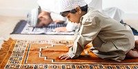 A young Arab boy in traditional attire prays on a prayer mat, showcasing devotion. The boy's focus on prayer highlights the importance of faith in daily life.