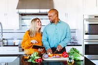 A happy couple, a Caucasian woman and an African American man, enjoy cooking together in a modern kitchen. They share smiles while preparing fresh vegetables and a meal. A happy couple vibes