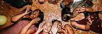 Group of diverse friends celebrating, lying on the floor with confetti. Smiling, joyful, diverse group enjoying a festive, colorful celebration together. Diverse friends celebrate festive party.