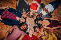 Diverse group of people lying on the floor, surrounded by confetti. Smiling men and women, various ethnicities, enjoying a festive celebration together. Drunk people at New year's eve party.