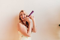 Smiling woman with blonde hair holding a purple party horn. Joyful expression, festive mood. Blonde woman enjoying a celebration with a party horn. Blonde girl celebrating at a party.