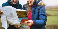 Elderly couple reading a map outdoors while traveling. Smiling elderly woman, old man with a beard. Exploring, map reading, and adventure in nature. Diverse old couple enjoy nature traveling with map