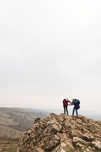 Three people hiking on a rocky mountain peak under a cloudy sky. Outdoor adventure, hiking, and nature exploration on a rugged mountain landscape. Elderly couple hiking hobby activity.