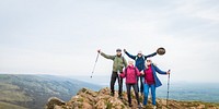 Group of four people hiking on a rocky hilltop, enjoying nature. They are dressed in outdoor gear, holding hiking poles, and smiling at the scenic view. Happy seniors hiking in British nature.