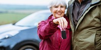 Elderly couple holding car keys, standing by a car. Outdoors, countryside. Senior man and woman, happy with new car. Car keys, new car, elderly couple, countryside. Old couple enjoy happy retirement. 