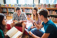 Group of young adults in a library, discussing books. Diverse group, engaged in conversation, surrounded by shelves of books, sitting on a red couch. Diverse high school students at library.