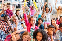 Diverse group of children in a classroom, smiling and raising hands. Kids engaged in learning. Happy, interactive classroom environment. Happy cute diverse elementary school kids.