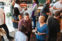 A diverse group of people socializing at a casual gathering. Men and women of various ethnicities are chatting and enjoying drinks in a lively atmosphere. People mingle at a busy social event.