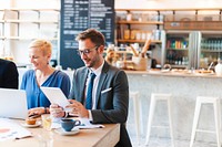 Two business people in a cafe, one using a tablet, the other a laptop. Bright modern setting with a casual business vibe. Modern productive workspace with diverse business people