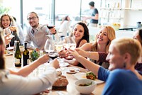 Group of people enjoying a meal, raising glasses in a toast. Diverse group celebrating, smiling, and dining together in a lively, cheerful atmosphere. Corporate party drinking and networking.