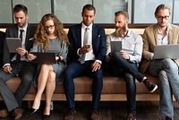 Group of professionals sitting on a couch, using devices like tablets and phones. Business attire, diverse team, technology and communication. Business people using digital devices, social media.