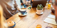 People at a wooden table with coffee, a laptop, and a plant. Casual meeting with coffee, and a laptop. Relaxed atmosphere with coffee and conversation. Casual business team working on project at cafe.