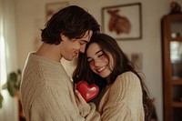 A caucasian man gives his girlfriend a red heart-shaped chocolate box sweaters happy smile.