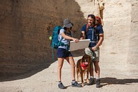 Two hikers with backpacks and a dog in a canyon. They study a map, planning their hike. Outdoor adventure with hikers, map, and dog in a canyon setting. Cute animal pet dog hiking with people.