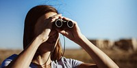 Woman using binoculars outdoors, focusing on distant views. Binoculars help in observing nature, exploring landscapes, and enhancing distant vision. Woman with binoculars, outdoor setting.