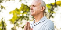 Elderly man meditating outdoors, eyes closed, hands in prayer. Peaceful meditation in nature. Relaxed elderly man enjoying meditation in a serene setting. Man fitness in park setting.