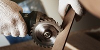 Close-up of hands using a circular saw to cut wood. The saw blade spins as it cuts through the wood. Protective gloves are worn for safety during the wood cutting process. Wood working photo concept.