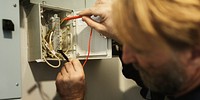 A man working on electrical wiring, adjusting cables in circuit box. Electrical work involves careful handling of wires and circuits. Focus on wiring and circuits. Electrician and industrial concept.