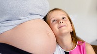 A young girl smiles, resting her head on a pregnant belly. The scene captures a tender moment of family, pregnancy, and childhood joy. Woman pregnancy, expecting baby concept. Girl and mother.