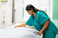 A healthcare worker in green scrubs makes a hospital bed. The medical professional is focused on patient care, ensuring a clean and comfortable environment. Hospital, medical, and healthcare concept.