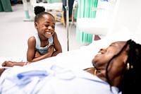 A child smiles at a person in a hospital bed, conveying warmth and care in a medical setting. The scene highlights family, health, and happiness. Hospital, medical, and healthcare concept.