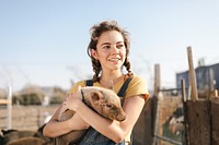 Young woman holding a piglet on a farm. Smiling woman with piglet, enjoying farm life. Farm setting with woman and piglet, showcasing rural lifestyle. Woman in farm lifestyle with pig animal.