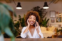 Smiling woman talking on phone, sitting indoors. Relaxed atmosphere with plants and cozy decor. Happy conversation, cheerful mood, bright smile. Woman using phone in cozy room portrait.