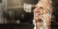 Man smiling while talking on a smartphone. Happy expression, casual setting. Close-up of a man enjoying a phone call, holding a smartphone. Business man in cafe portrait, having conversation.