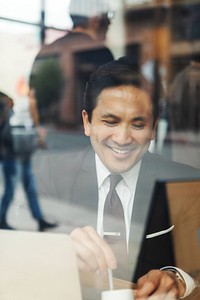 Smiling man in a suit working on a laptop in a cafe. Businessman enjoying work, focused on screen. Professional setting, urban environment, positive mood. Business man in cafe portrait.