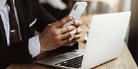 Person using smartphone and laptop at a desk. Hands holding phone, laptop open. Technology use, multitasking. Office setting, digital devices in use. Digital devices of business person in cafe.