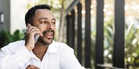 Man talking on phone outdoors, wearing a white shirt. Relaxed conversation, enjoying a sunny day. Greenery in the background, casual setting.  A man using a smartphone, conversation.