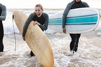 Two people in wetsuits carrying surfboards at the beach. Surfboards in hand, they enjoy the ocean waves. Surfboards and wetsuits are essential for surfing fun. Extreme sports and adventure travel.