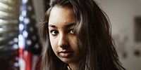 A woman looking at the camera with American flag in the background. Photo of Asian woman portrait. Portrait of a south Asian girl looking at the camera with the United States flag in the background.