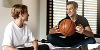 Two young males sitting indoors, one holding a basketball. They are casually dressed, smiling, and appear to be enjoying a relaxed moment together. Caucasian brothers photo.