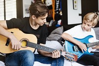 Two boys playing guitars in a cozy room. One with an acoustic guitar, the other with an electric guitar. Casual setting, focused on music and practice. Caucasian brothers photo.