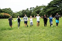 Diverse group of people holding hands in a park. Men and women of various ethnicities enjoying nature. Smiling, unity, and outdoor fun in a green field. Diverse people group in park outdoor.