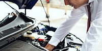 Man in a white shirt and tie checks a car engine. Car maintenance, engine inspection, and repair. Focus on car engine and maintenance work. Car and vehicle maintenance photography.