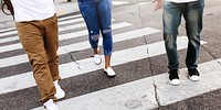 Three people walking on a crosswalk, wearing casual jeans and sneakers. Urban street scene with diverse individuals in casual attire, crossing the street. Three people crossing road.