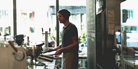 A barista in a beanie works in a cafe, preparing drinks. The cafe setting is cozy, with coffee equipment visible. The barista is focused on their task. Barista man behind cafe counter.