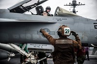 U.S. Navy Airman Christopher BazanKoury signals the pilot of an F/A-18E Super Hornet aircraft assigned to Strike Fighter Squadron (VFA) 27 on the flight deck of the aircraft carrier USS George Washington (CVN 73) in the Philippine Sea July 8, 2014.