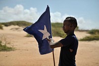 A young man carries the Somali flag while leading a group of soldiers during a demonstration by a local militia, formed in order to provide security in the town of Marka, Somalia, on April 30. AU UN IST PHOTO / Tobin Jones. Original public domain image from Flickr