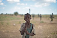 A young boy poses for the camera as Burundian trooops, part of the Afrian Union Mission in Somalia, patrol the countrside behind him near Mahaday town in the MIddle Shabelle region of the country. AMISOM Photo / Tobin Jones. Original public domain image from Flickr